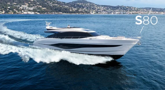 "Princess-s80" Stylish yacht Princess S80 cruising along a coastal area with a scenic town and hillside in the background.